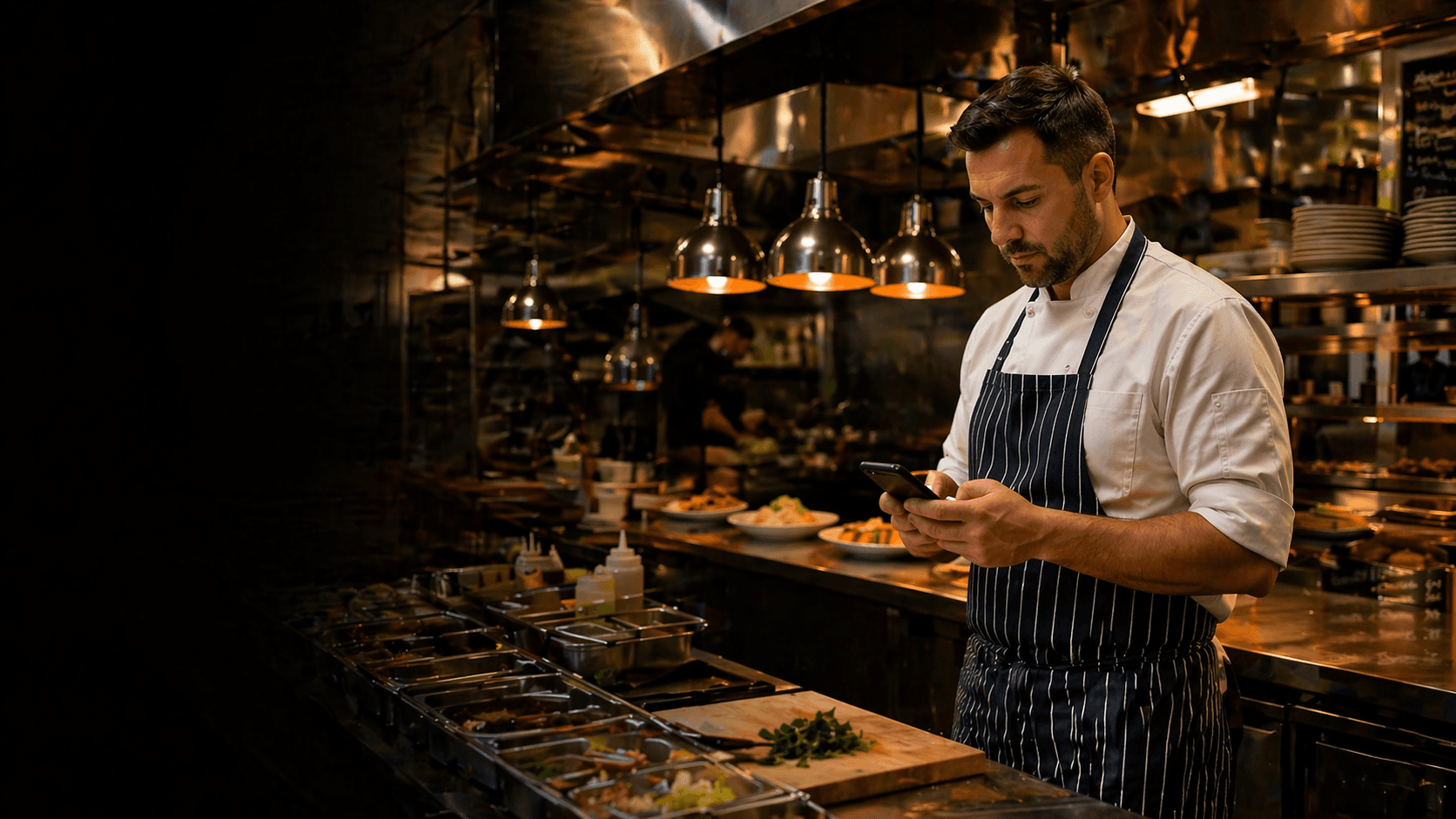 Restaurant chef using a phone in a professional kitchen without text overlay.