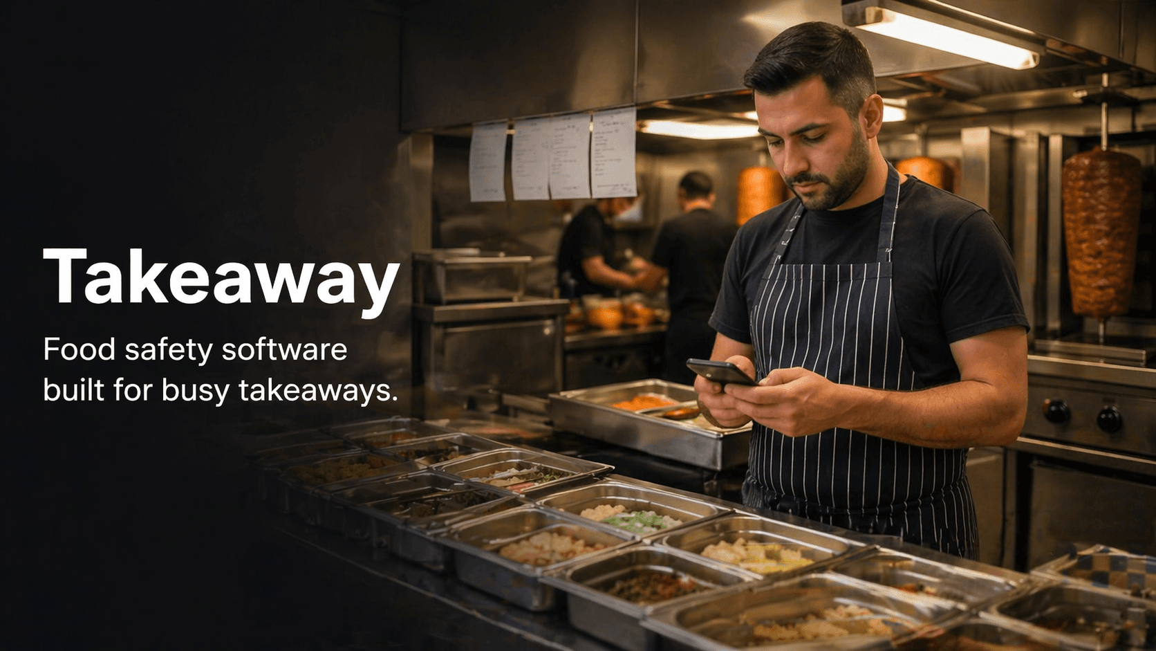 Takeaway staff member using a phone in a busy kitchen while completing a food safety check.